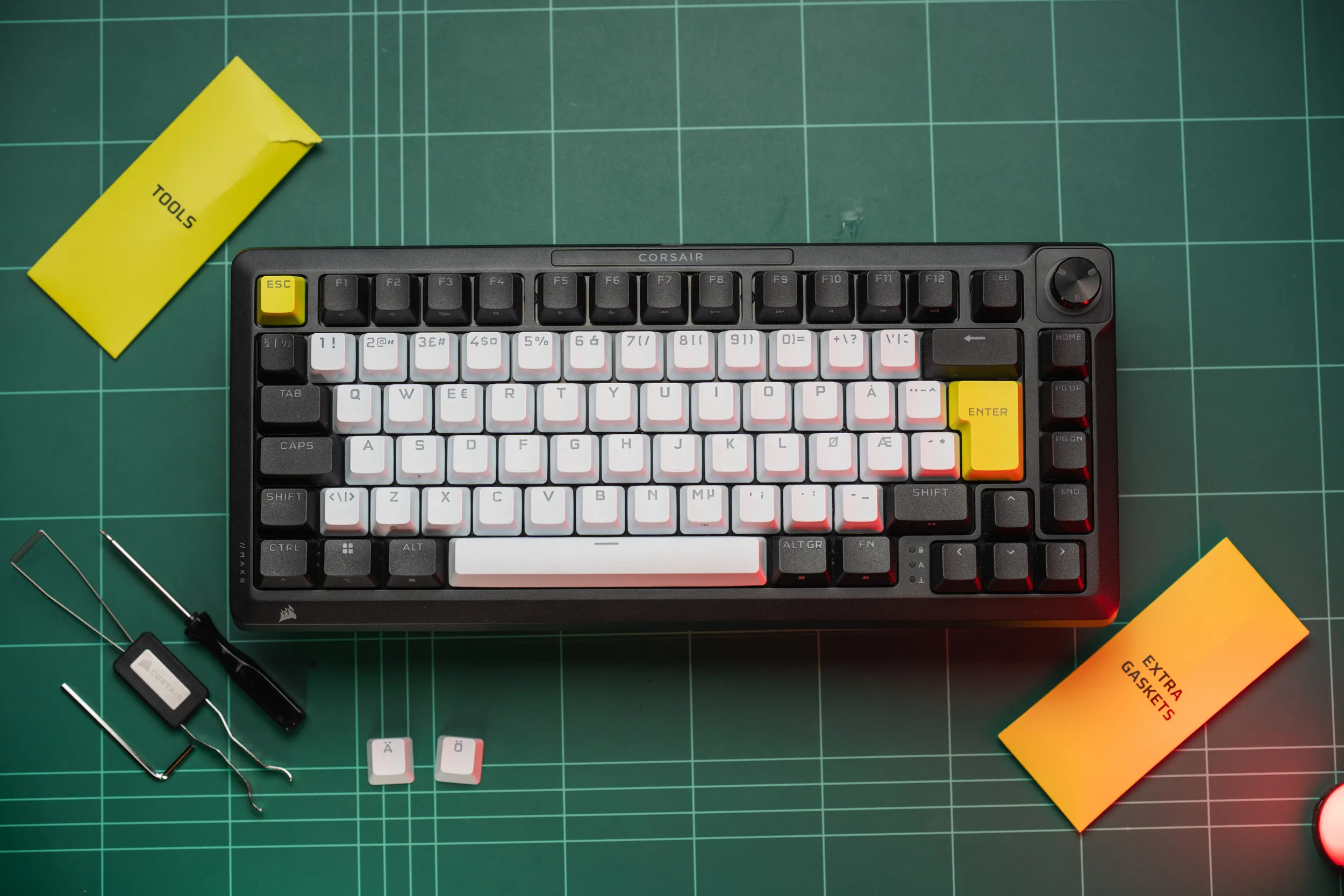 Corsair MAKR PRO 75 på en grønn skjærematte med medfølgende verktøy, de merkede verktøy- og pakningskonvoluttene, og de ekstra nordiske keycapsene