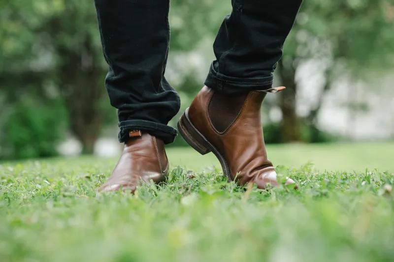 Brune R.M. Williams Comfort Craftsman til sorte jeans, lav vinkel på grønt gress