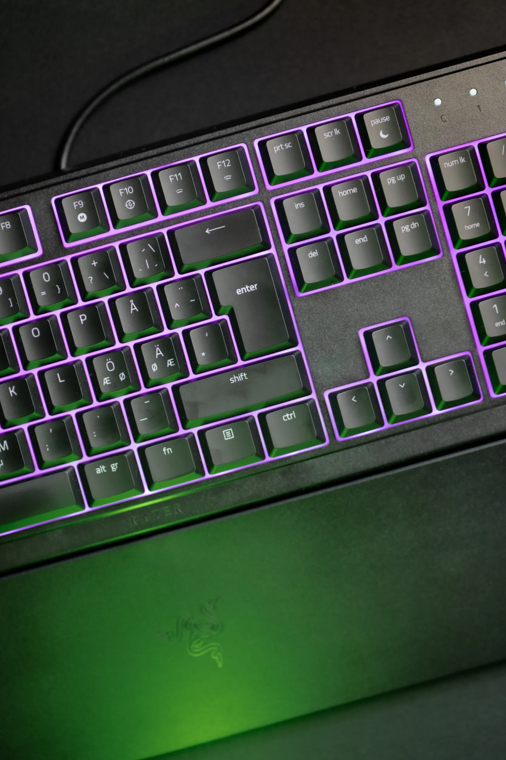 Nærbilde av høyre side av Razer Ornata V3 X med tastene opplyst i lilla Chroma RGB og et grønt skjær under