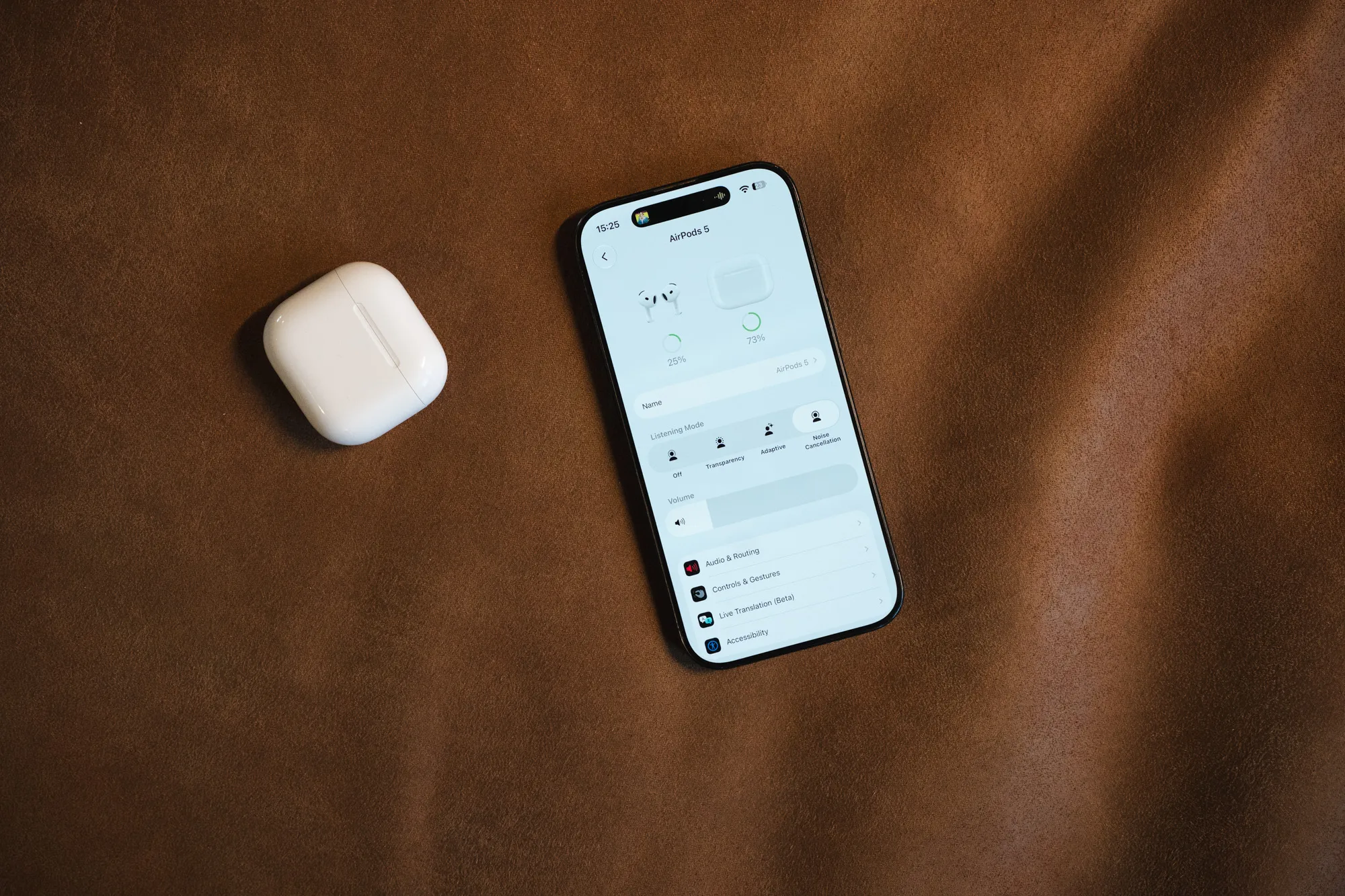 AirPods 5-etuiet og en iPhone med AirPods-innstillingene på et brunt skinnunderlag, sett ovenfra