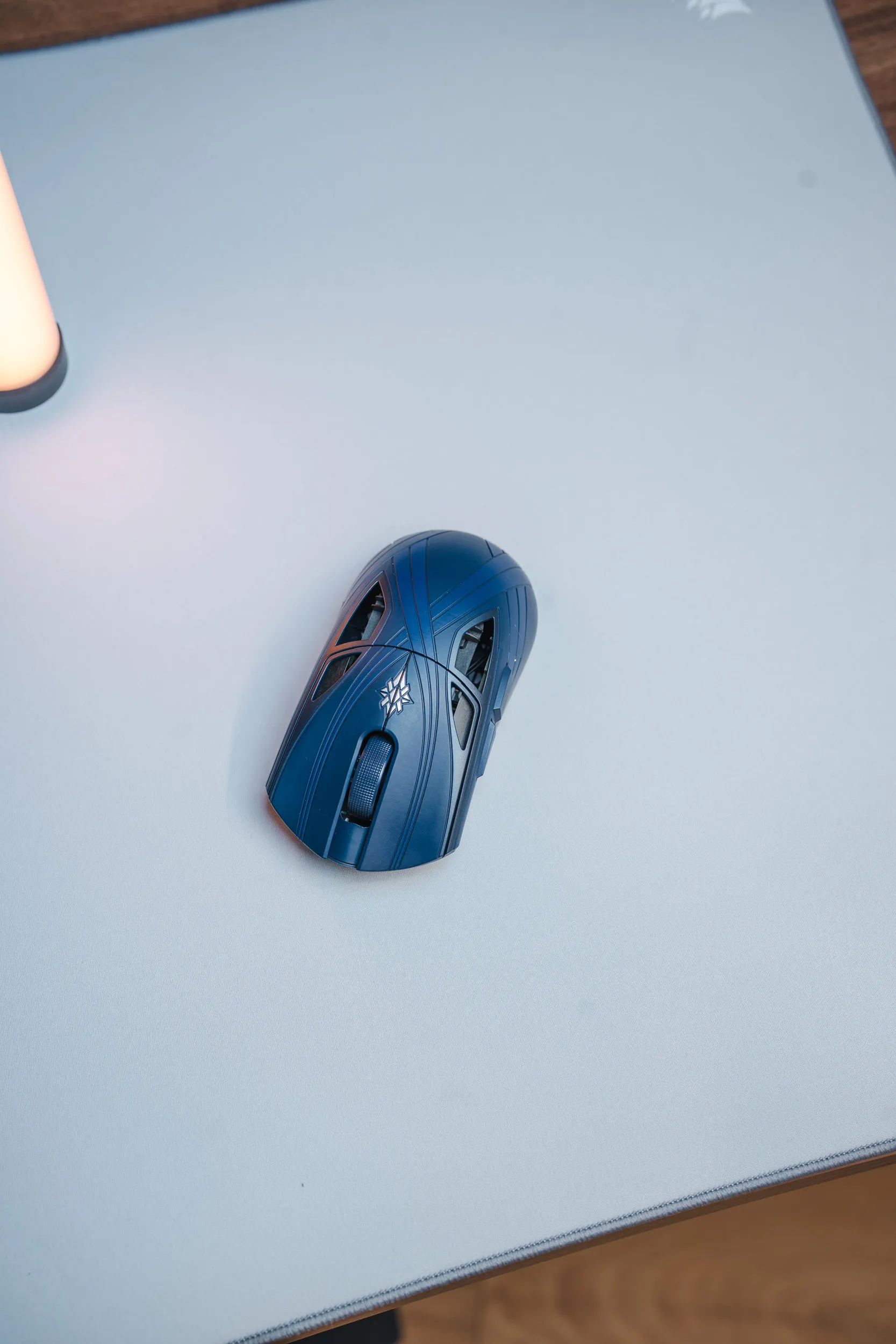 Finalmouse SLX Nightfall sett ovenfra på en lys musematte, med symbolet bak scrollhjulet og åpninger i skallet over begge knappene