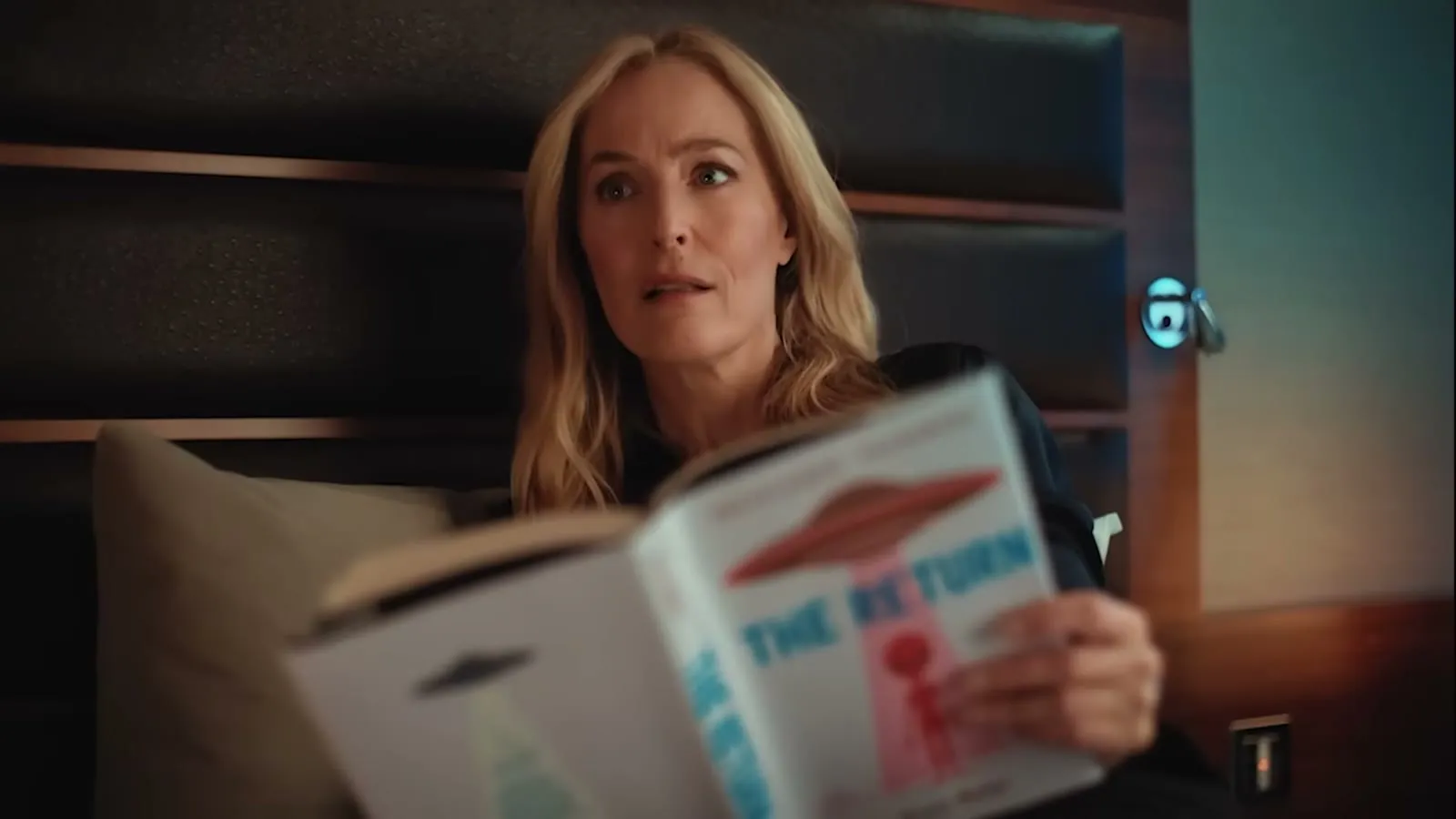 Gillian Anderson i en hotellseng med et blad med UFO på forsiden