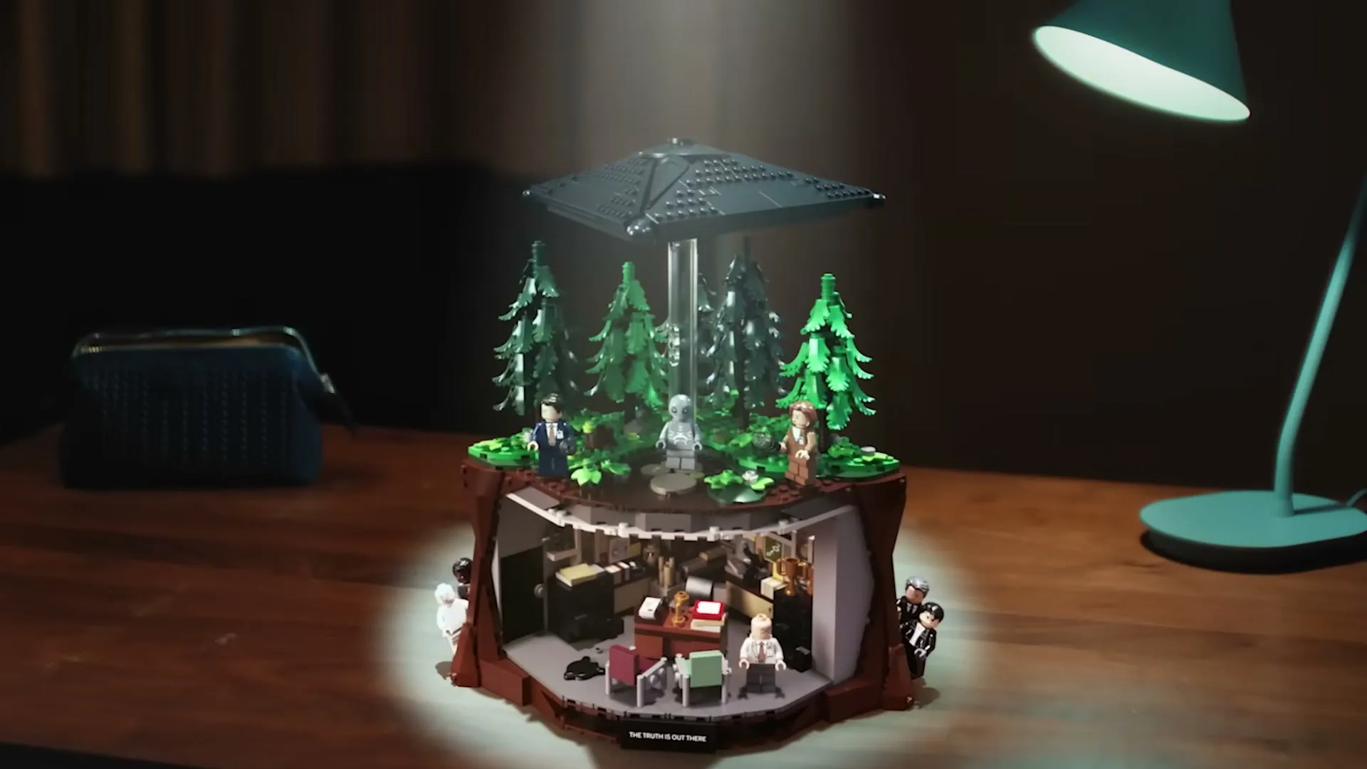 Det ferdige LEGO-settet av X-Files på et skrivebord, med kontoret nederst og UFO-en over skogen
