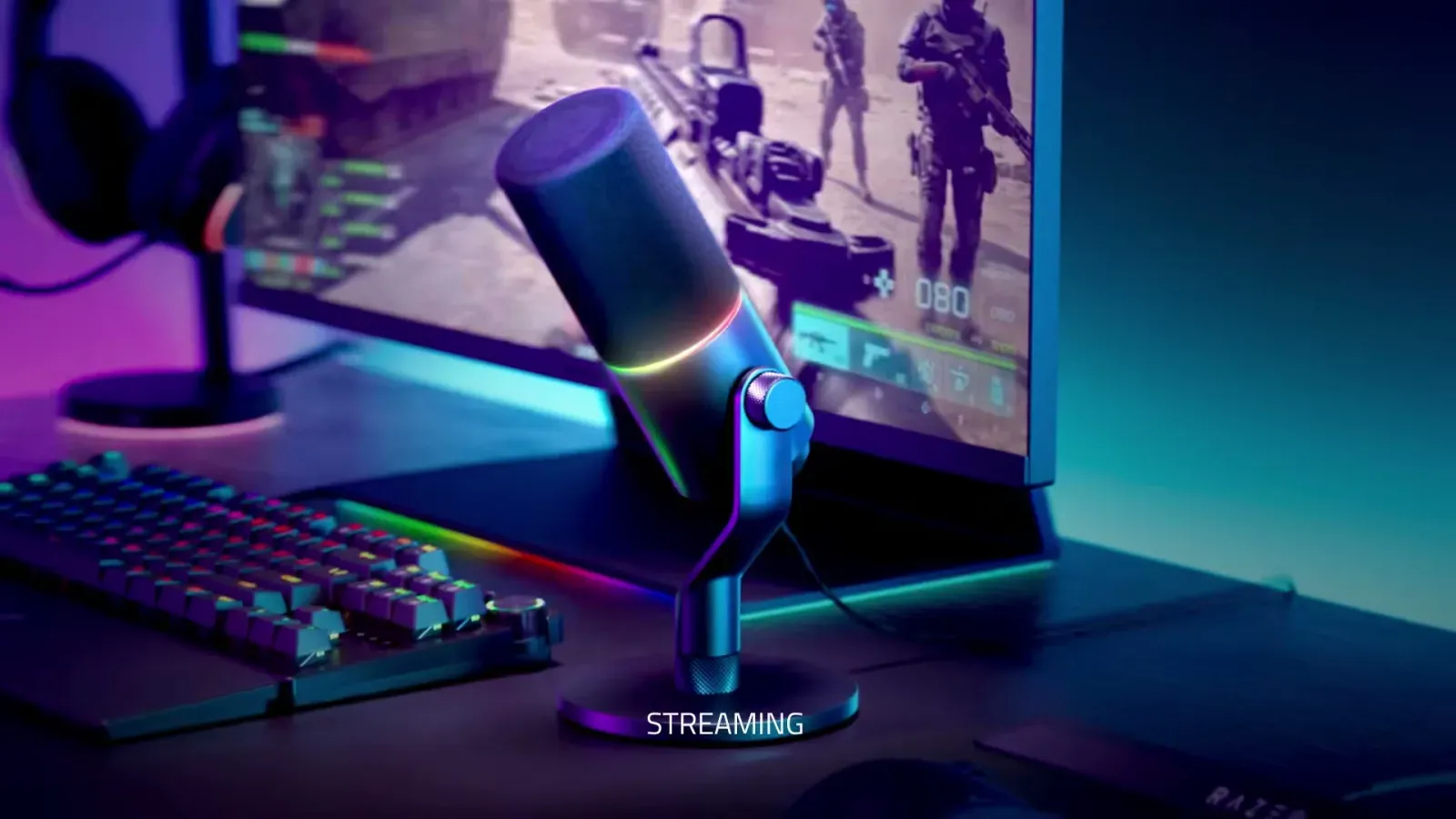 Razer Seiren V3 Pro på bordstativ ved et gamingoppsett med tastatur og skjerm