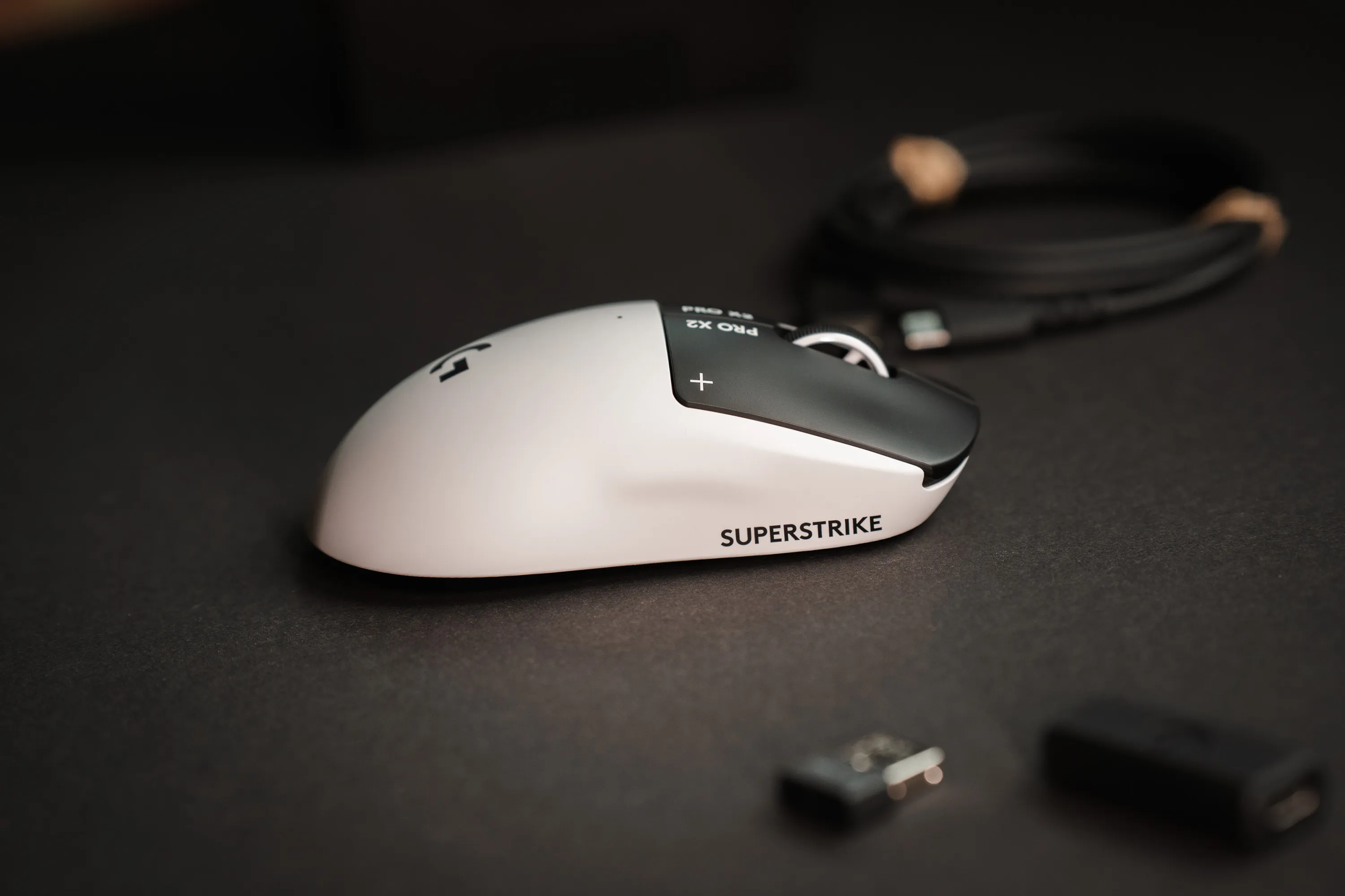 Logitech G Pro X2 Superstrike på pulten med mottakeren og adapteren i forgrunnen